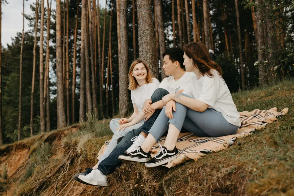 Three friends sitting together on a blanket in a pine forest